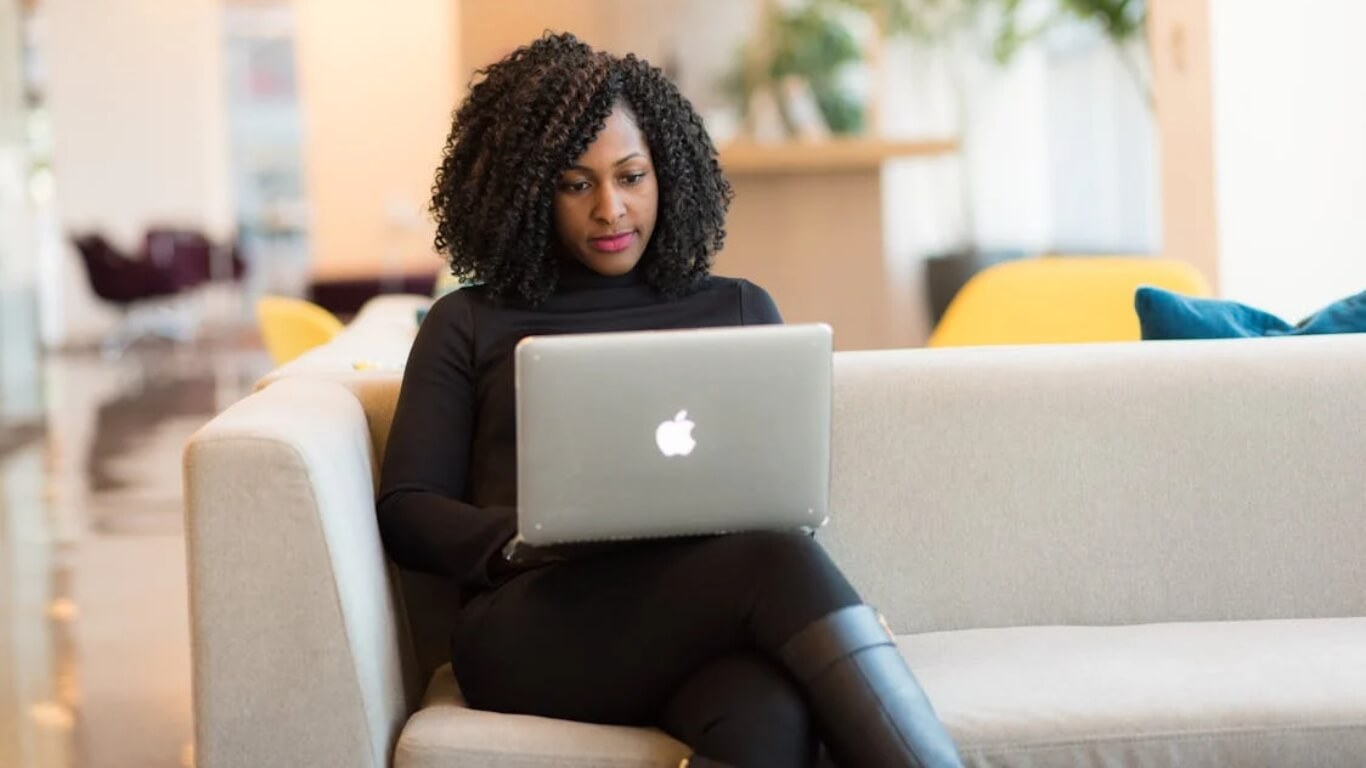 Entrepreneur using a MacBook on a white couch, researching business insurance options for startups